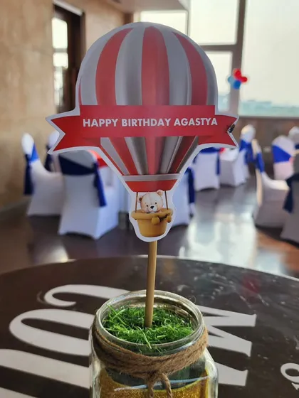 Another style of table centerpiece for the hot air balloon party. This one features a personalized cutout with a teddy bear peeking out of the balloon basket, adding a playful touch.