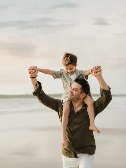 A father gives his son a shoulder ride on the beach at sunset. This classic pose creates a beautiful silhouette and a feeling of freedom.