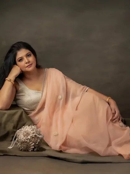 Reclining in the softness of a peach silk saree. This painterly portrait is all about quiet grace and the glow of self-assurance, proving that beauty shines from within.