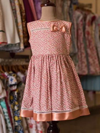 This pink printed dress is finished with a satin ribbon hem and a delicate bow at the neckline. It's a beautiful example of a simple design elevated by thoughtful details.