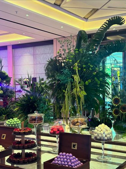 Another view of the incredible dessert display, where sweets are presented in elegant glassware and wooden boxes, surrounded by a jungle of green.