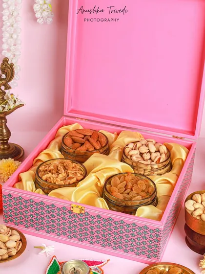 An open view of the pink Diwali hamper, revealing the neatly arranged jars of dry fruits on a bed of golden silk. This shot emphasizes the premium quality of the gift.