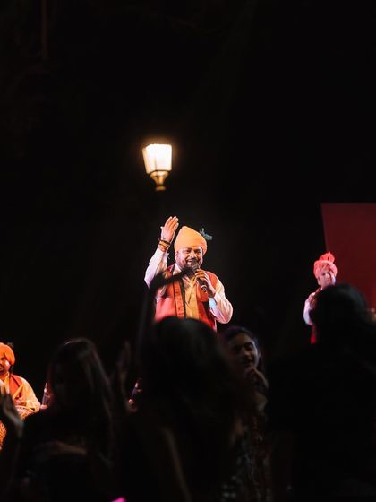 A singer in a turban performs for an engaged crowd, framed by a classic street lamp. This shot captures the unique ambiance of an outdoor evening performance in Delhi.