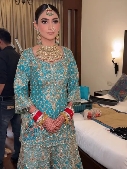 A full-length view of the bride in her beautiful turquoise sharara. The makeup perfectly complements the unique color of her outfit.