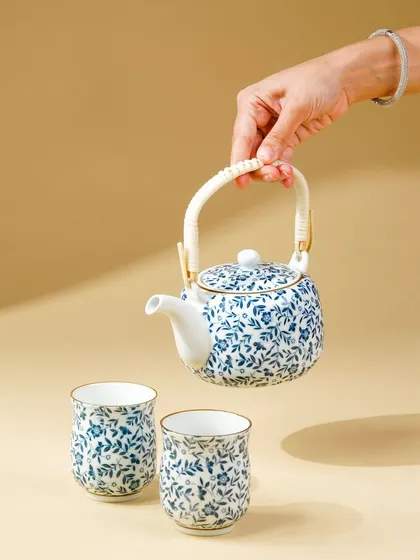 A minimalist shot of a hand holding a beautiful, hand-painted ceramic teapot. The focus on the product against a clean background highlights its delicate craftsmanship.