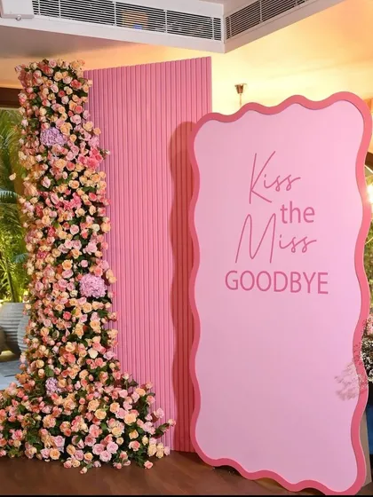 A chic and modern 'Kiss the Miss Goodbye' floral backdrop for a bridal shower, featuring a pillar of pink and peach roses.