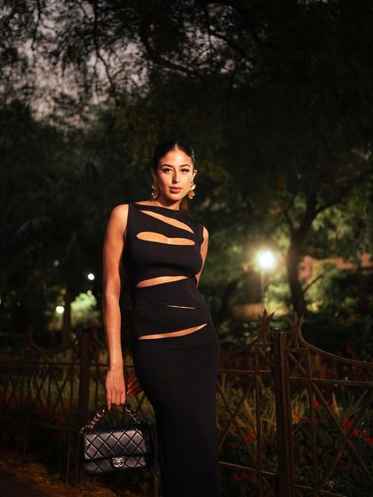 An outdoor evening shoot for an H&M x Mugler collaboration. The dramatic lighting and the model's pose highlight the unique cut-out details of the black dress, creating a chic and sophisticated fashion statement.