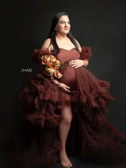 So much glamour in one photo. This mom-to-be looks incredible in a ruffled, high-slit brown gown against a classic dark backdrop, creating a powerful and elegant portrait.