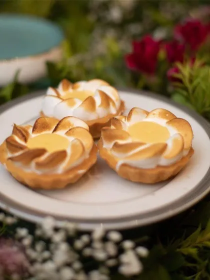 A close-up of our lemon meringue tartlets, nestled in a bed of greenery. The perfectly torched meringue and buttery crust showcase the fine details of our pastry work.