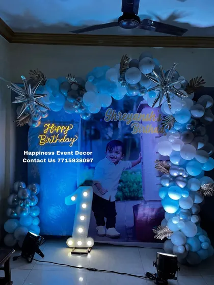 A cool blue and silver themed decor for a first birthday at home. This setup uses a personalized photo backdrop, a balloon arch with starburst foil balloons, and a neon sign.