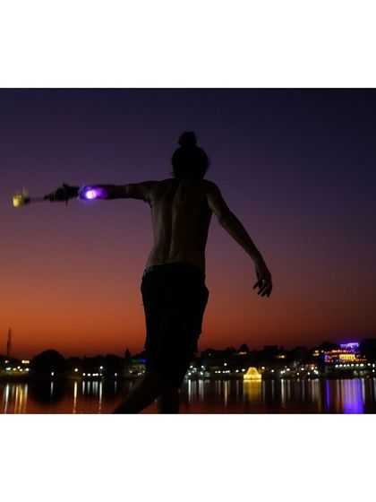 Another angle of the juggler in Pushkar, capturing the motion of his body and the glowing sticks against the deep purple and orange of the twilight sky.