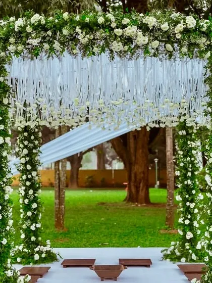 The clean lines and lush florals of this outdoor mandap create a space that is both simple and stunning. The hanging white ribbons add a touch of delicate movement against the green backdrop.