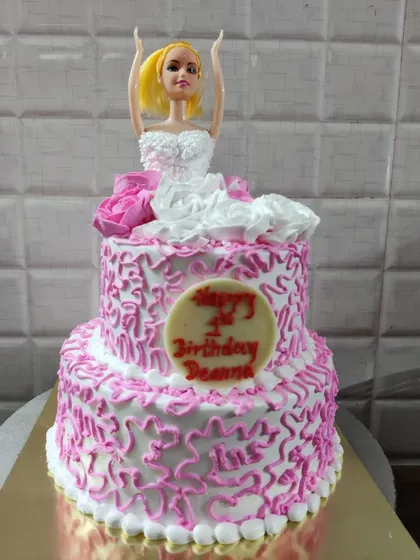 A two-tier doll cake for Deanna's first birthday. The design features a white and pink dress with intricate piping details.