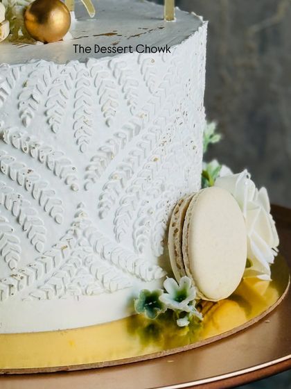 Another detail of the white stenciled anniversary cake, showing the intricate leaf pattern and the placement of the French macaron.