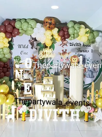 A "Wild and Classy" jungle safari theme with muted green and brown balloons. The picket fence and light-up name add a rustic charm.