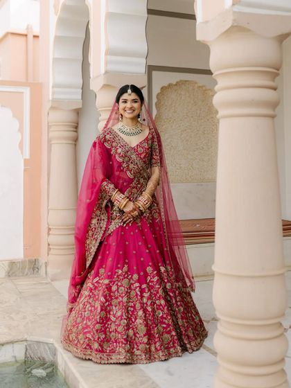 Posing against the beautiful architecture in Jaipur, this bride's vibrant lehenga and glowing makeup create a truly memorable wedding day portrait.