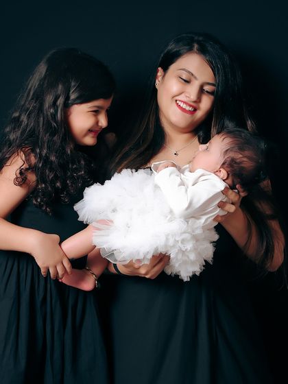 A portrait of sisterly and motherly love. The older sister looks on with adoration as her mother holds the new baby, creating a beautiful memory of the girls in the family.