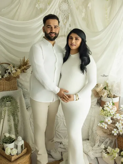 A simple and classic portrait of an expecting couple. Dressed in white against a white backdrop, the focus is entirely on their happy expressions and the baby bump they cradle together.