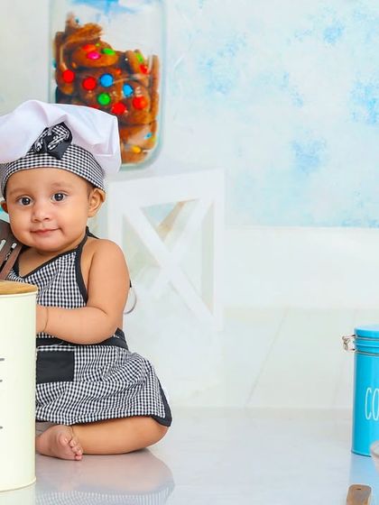 Our little chef is proudly showing off his cooking tools. The setup includes cute kitchen canisters and colorful ingredients for a playful scene.
