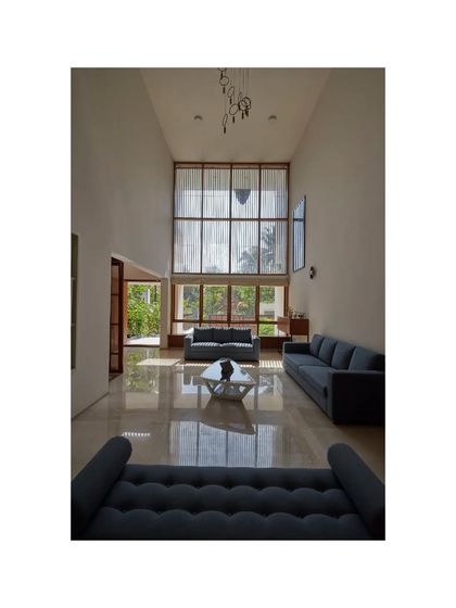 A wide shot of the living area in the Vikas Residence, showing the grand scale of the double-height space and the simple, elegant furniture arrangement.