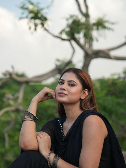 A simple and natural outdoor portrait of a model in a black suit, sitting on a rock with greenery in the background.