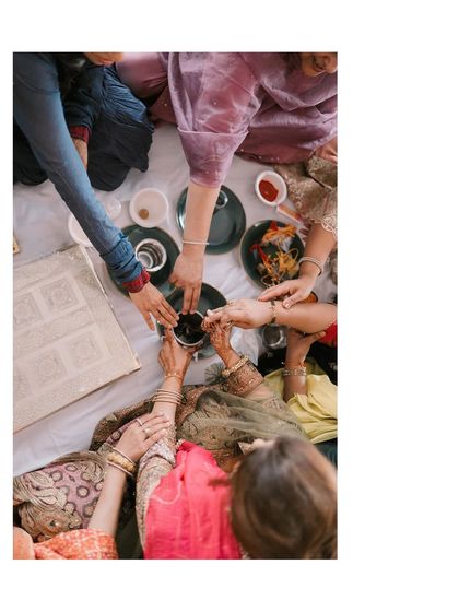A close-up of a Mehendi ritual. This overhead shot инновационно captures the tradition and the community of women participating in the ceremony.