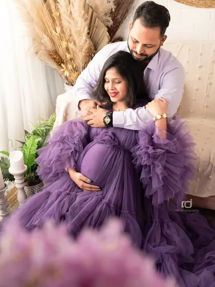 A loving embrace on a comfortable studio sofa. The rich purple gown and soft surroundings create a cozy and romantic setting for this couple's portrait.