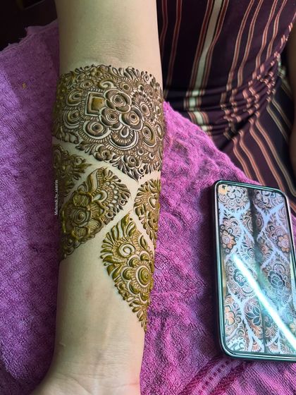 A close-up of the forearm, showing the intricate details of the designer pattern. The reference photo is visible on the phone.