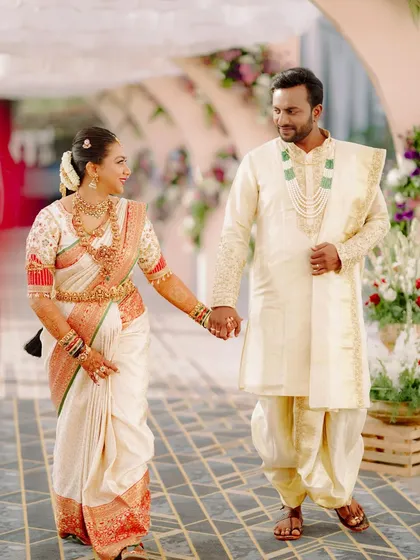 For this beautiful wedding, I designed a coordinated look for the couple. The bride's classic off-white and red Kanjeevaram silk saree is perfectly matched by the groom's cream-colored sherwani and dhoti, creating a timeless and elegant wedding day style.