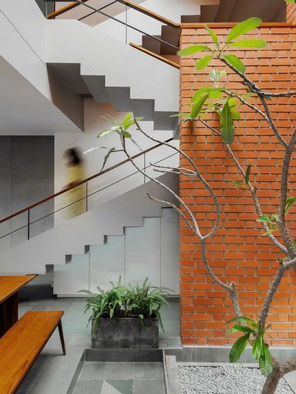 The main staircase wraps around the brick-clad wall of the internal courtyard. The play of light and shadow from the skylight above, combined with the motion of someone using the stairs, creates a dynamic and ever-changing scene.