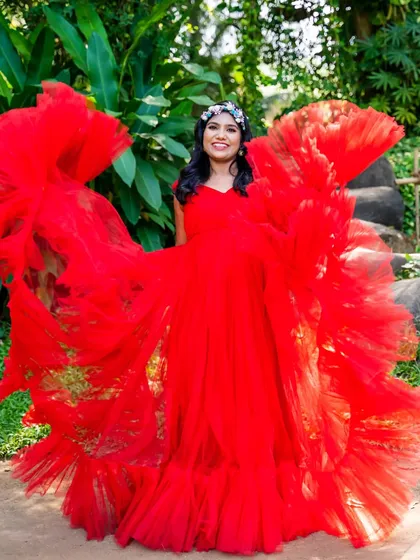 A joyful, vibrant portrait. The mom-to-be is surrounded by the ruffles of her bright red gown, looking like a beautiful flower in bloom.
