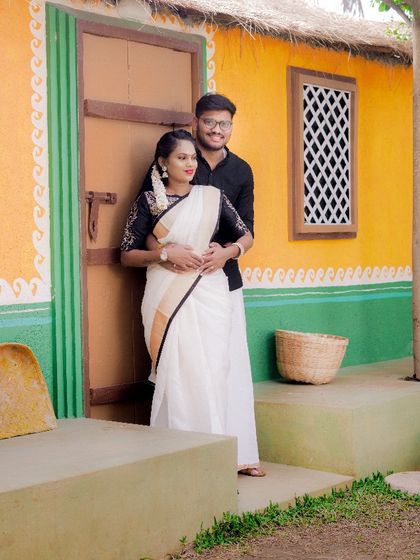 A sweet embrace in front of a traditional village house set. The couple's classic black and white outfits look timeless against the colorful walls.