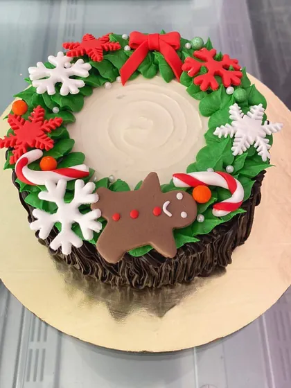 A festive Christmas wreath cake, complete with a gingerbread man, candy canes, and snowflakes.