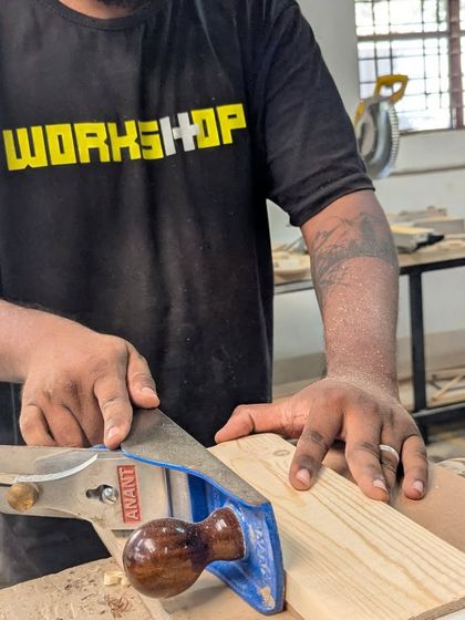 Using a hand planer to smooth the surface of a pine board. Even in our power tool workshop, we mix in essential hand tool skills for that perfect finish.