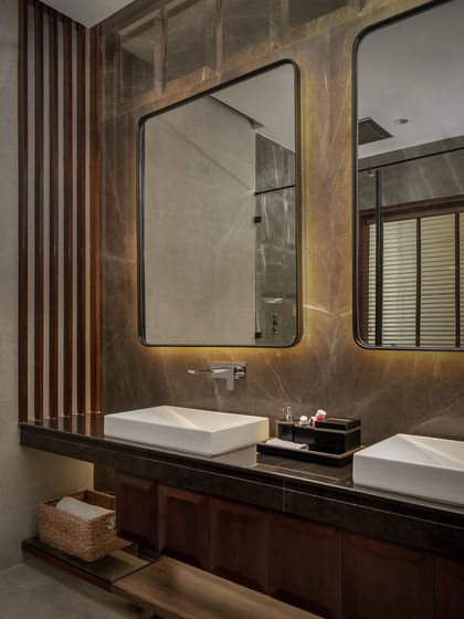 An organic, warm bathroom with earthy brown stone walls and LED backlighting behind the mirrors. A tucked-in sculpture adds a curated, personal touch to this immersive space.