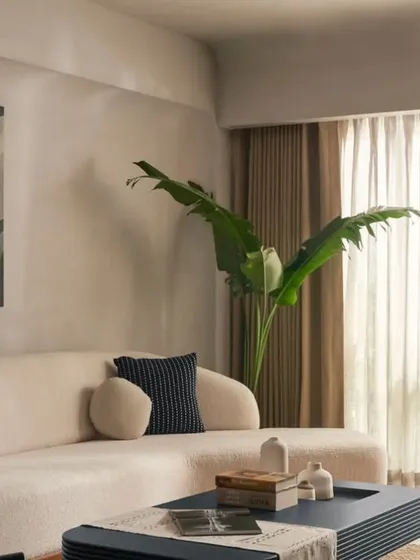 An ivory boucle sofa sits against a light grey lime-washed wall, creating a soft and inviting corner. The abstract art adds a touch of modern personality to the serene, minimalist living room design.