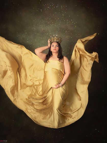 A dramatic and artistic pose showing off the beauty of pregnancy. The mom-to-be is captured from above in a flowing golden gown, looking powerful and serene.