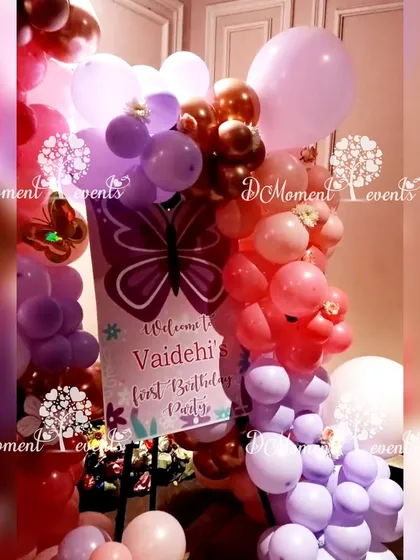 A welcome sign for Vaidehi's first birthday, framed with a beautiful arrangement of red and purple balloons.
