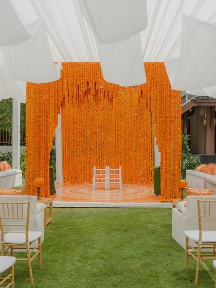 A wide view of the Haldi ceremony space, with a canopy of white drapes, a marigold stage, and elegant guest seating.