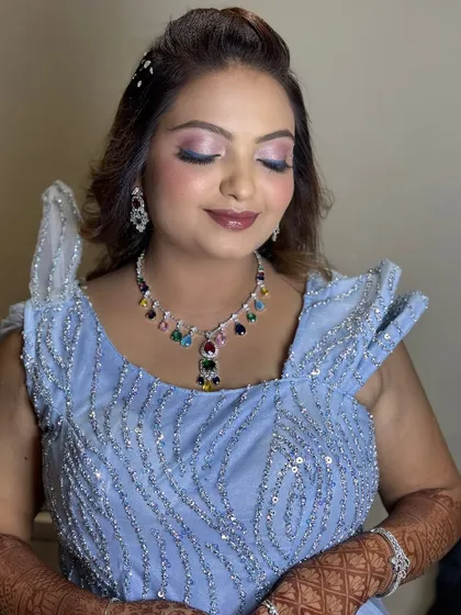 A modern reception look in a powder blue gown with a colorful statement necklace and shimmery eye makeup.