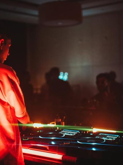 A DJ seen from behind, looking out at the dance floor. The red lighting and focused energy capture the essence of a night at The Park Ballroom.