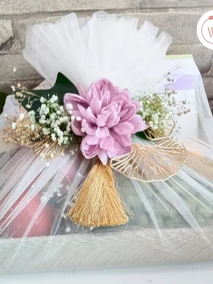 A stunning hamper in purple and white, featuring a mix of traditional treats and a modern Armani Exchange watch. The gift is elegantly wrapped in white tulle with a large purple flower.