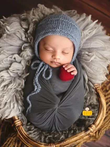 A simple and powerful portrait. The baby is wrapped in grey, holding a small red heart, creating a beautiful contrast against the textured basket.