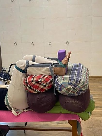 An advanced therapeutic setup for deep relaxation and hip opening. The body is completely supported by a bench, bolsters, and belts.