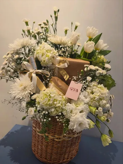 There is a timeless elegance to a classic floral gift. This beautiful wicker basket is overflowing with fresh white hydrangeas, tulips, and chrysanthemums, with carefully wrapped presents nestled within for a sophisticated birthday surprise.