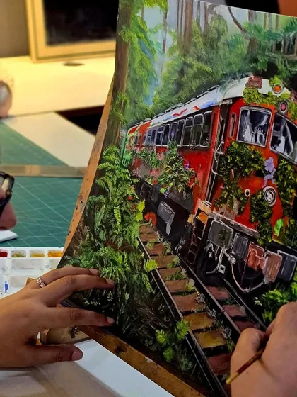 An over-the-shoulder view of a student working on her gouache painting. Her palette is visible, showing the colors she is mixing to create the scene.