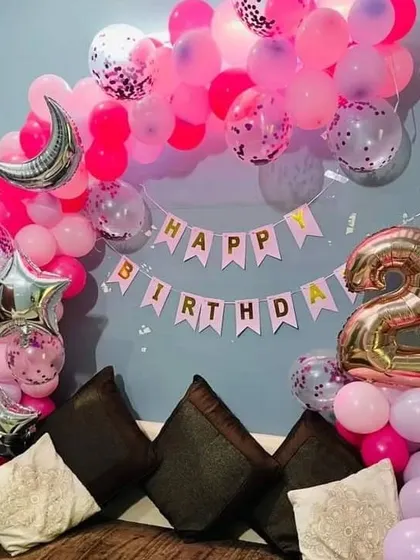 A simple and sweet pink-themed 2nd birthday decoration for home. This setup includes a balloon arch over a sofa, a "Happy Birthday" banner, and star and moon foil balloons.