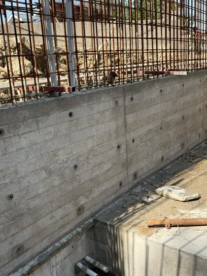 A board-formed concrete wall under construction. The wooden planks used in the formwork leave their grain imprinted on the concrete, adding a layer of natural texture.