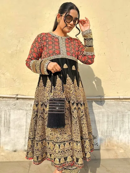 A detailed shot highlighting the texture of the black beaded potli against the intricate gold and red embroidery of the suit.