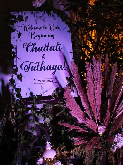 A simple and elegant welcome sign, beautifully lit in purple and surrounded by pampas grass, for a chic and modern evening event.